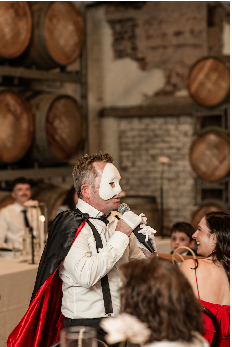 Jon Bode in a Phantom mask singing beside a laughing guest during a live winery performance